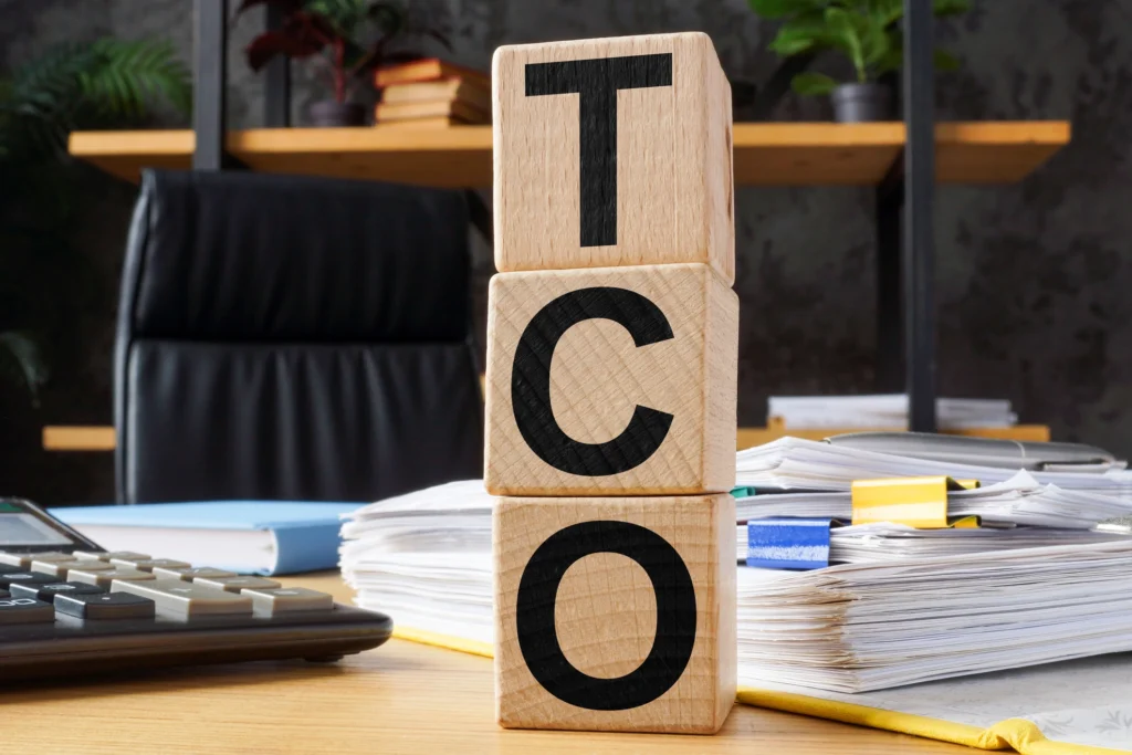Stacked wooden blocks labeled TCO on a desk, symbolizing total cost of ownership analysis used to evaluate facility coating system ROI.