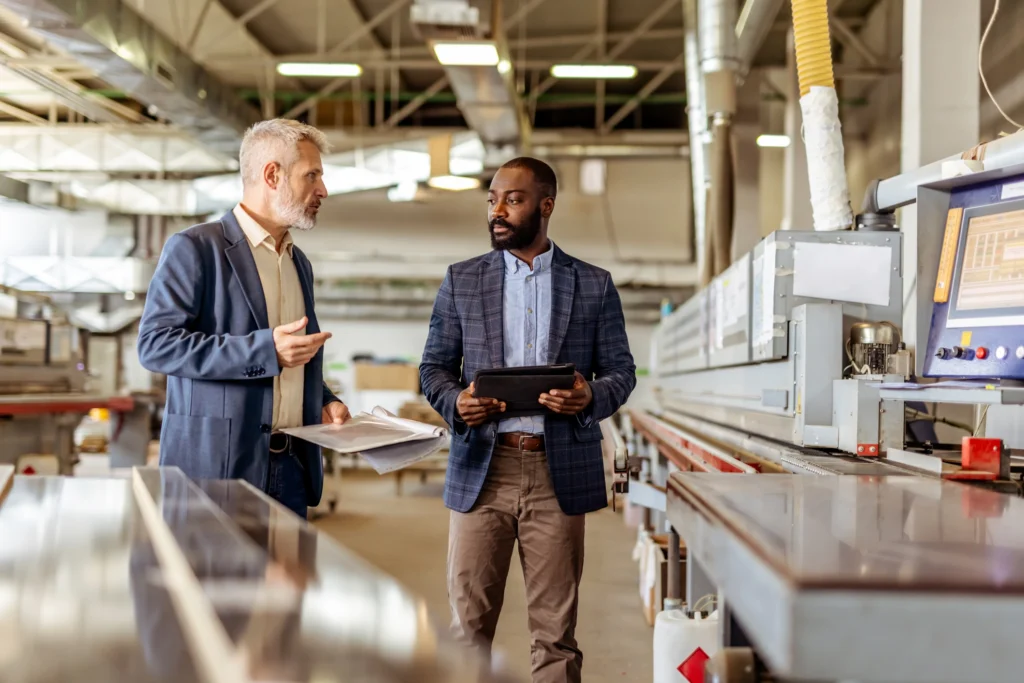 Facility managers reviewing operations on a production floor, demonstrating how coating system decisions affect downtime, labor efficiency, and compliance planning.