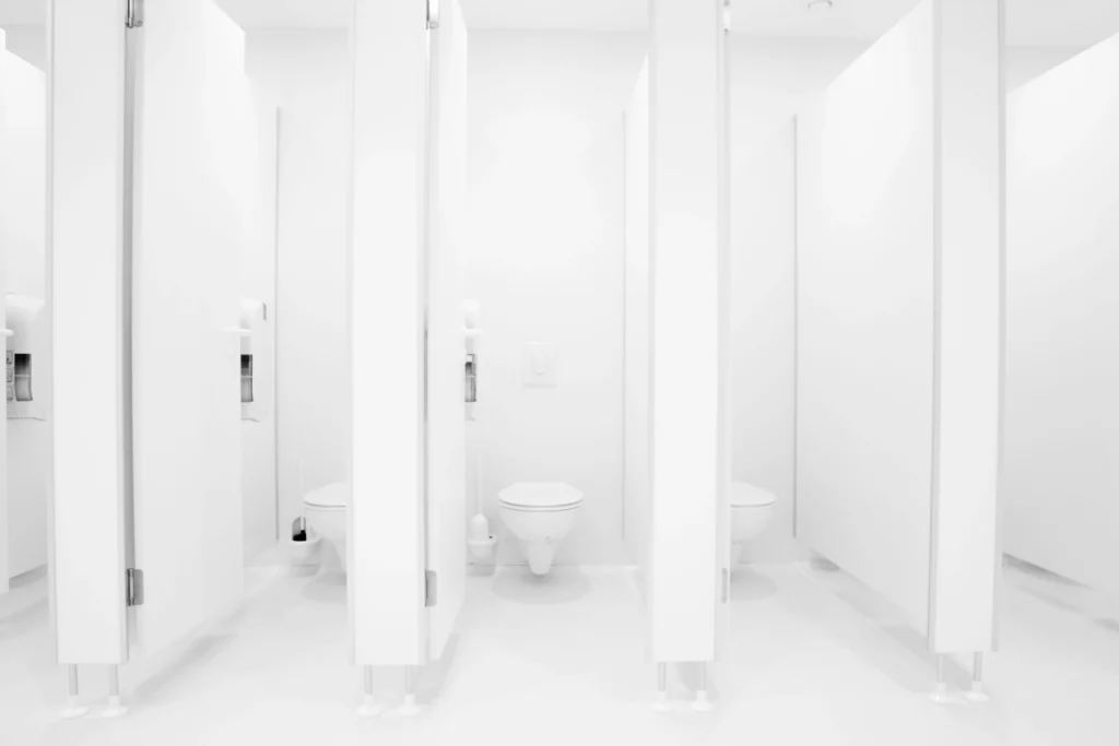 White public restroom toilet stalls with smooth walls and floors designed for durability and easier cleaning in high-traffic facilities.