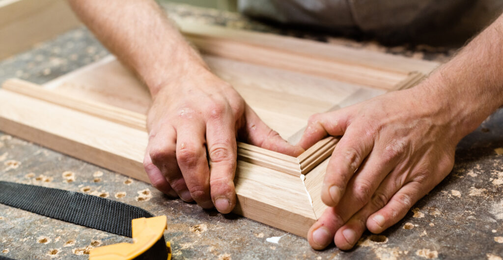 Wood worker holding together two wood pieces with glue on the sides
