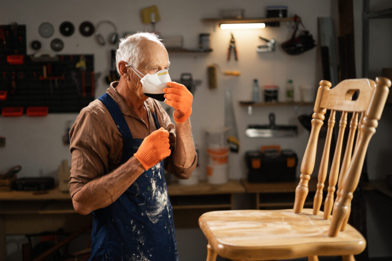 Older craftsman with white hair wearing protective mask and gloves to avoid inhaling any fumes from his work